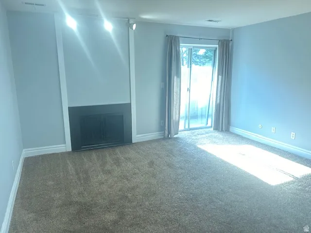 Built-in fireplace with black surround, track lighting, light blue wall paint, plush carpet flooring, and a sliding glass door