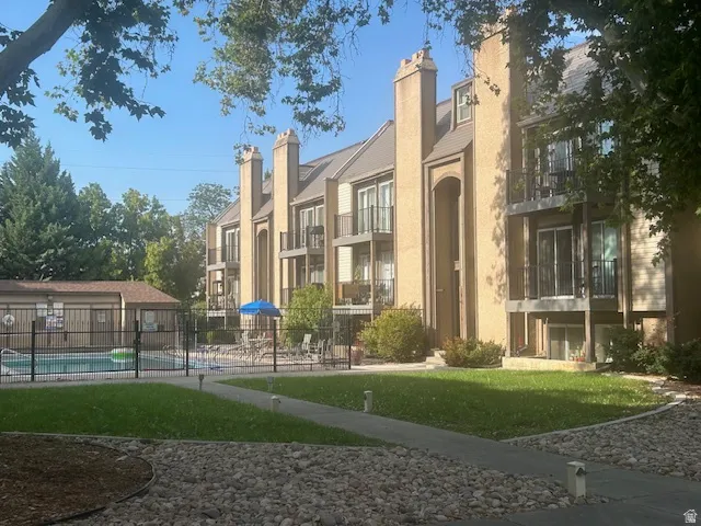 Multi-story building featuring balconies with sliding glass doors, a fenced swimming pool, and dedicated green spaces with walkways