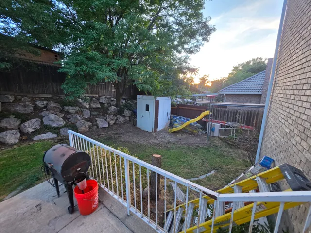 Terraced landscaping with a rock wall, mature tree, and a shed