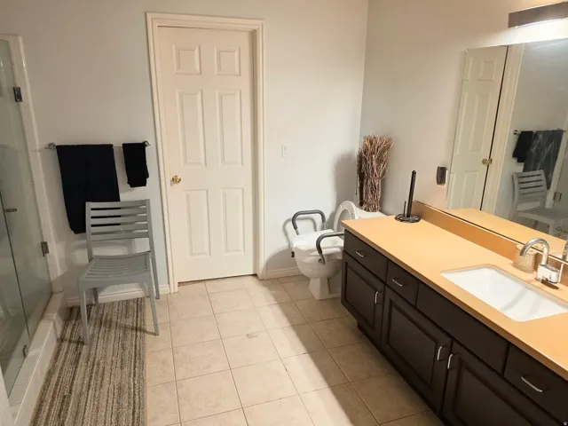 Tile flooring, vanity with integrated sink, expansive mirror, glass-enclosed shower, panel door