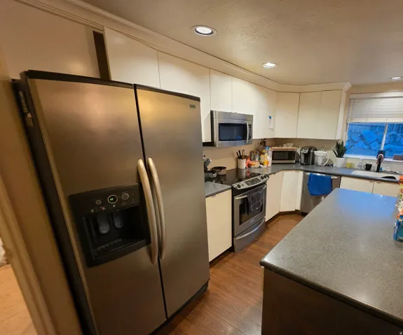 Stainless steel side-by-side refrigerator, recessed lighting, wood-finish flooring, white cabinetry, and a dark countertop on the island