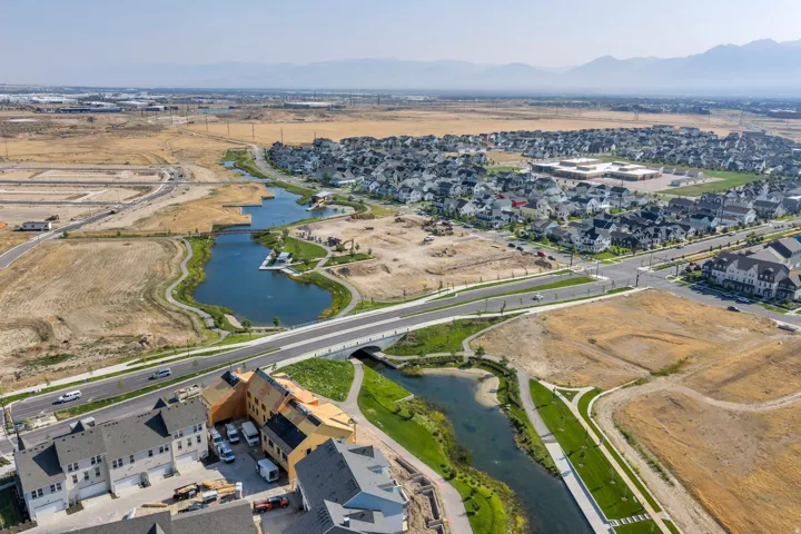 Aerial perspective featuring a residential community, a prominent body of water with docks, a paved pedestrian pathway, and a bridge crossing a waterway