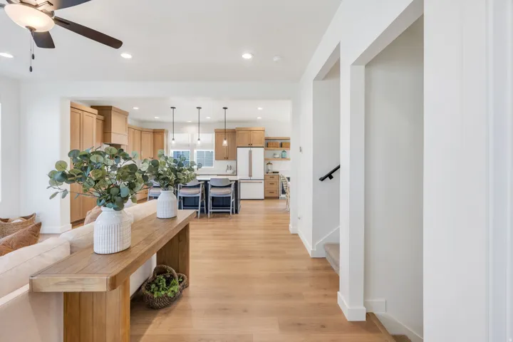 Light wood-finish flooring throughout, recessed lighting, ceiling fan, and staircase with a black handrail
