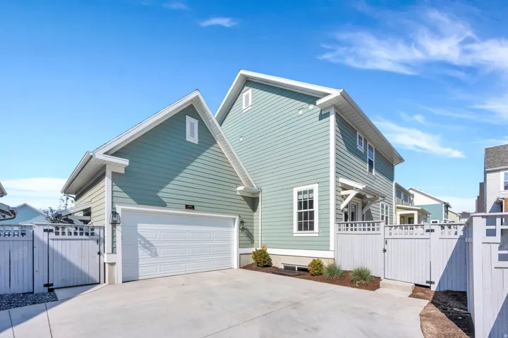 Light blue siding exterior with white trim, attached two-car garage, concrete driveway, white privacy fencing, and exterior lighting fixtures