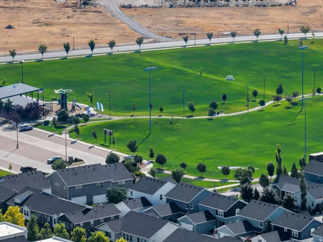Expansive green park with a playground, covered picnic area, and paved pathways, bordered by residential properties