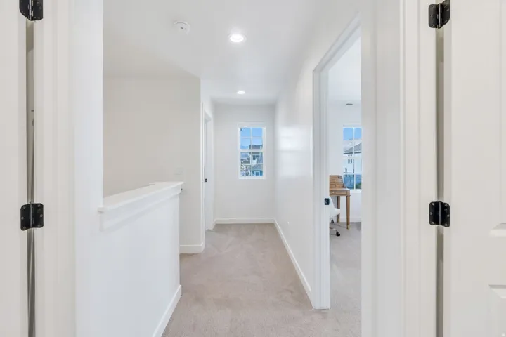 Carpeted hallway with white walls, recessed lighting, and a window with white trim