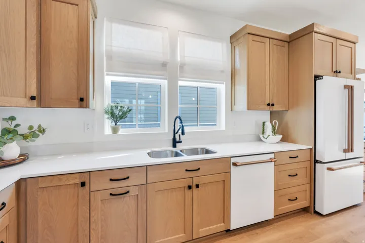 Light wood-finish cabinetry with black hardware, white countertops, built-in stainless steel sink with a matte black faucet, and hardwood flooring