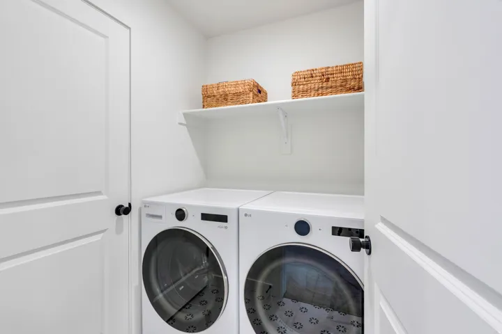 Dedicated laundry area featuring a white floating shelf, white walls, and built-in appliances