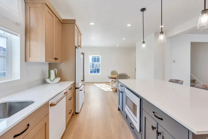White countertops, wood-finish flooring, recessed lighting, and kitchen island with pendant lighting