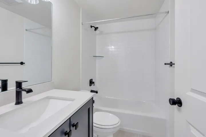 Bathroom featuring a white subway tile shower surround, dark vanity with white countertop, matte black fixtures, and wood-finish flooring