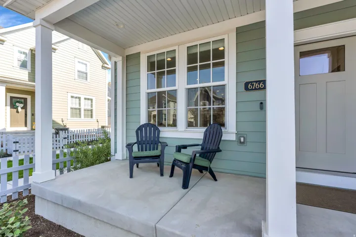 Covered front porch with concrete flooring and white columns, featuring a beadboard ceiling and light green siding