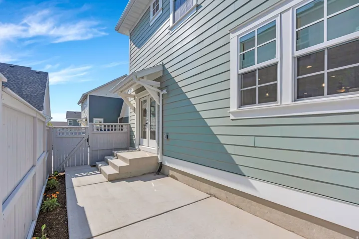 Exterior siding in a light tone, white-framed windows, concrete patio, concrete steps, and a white gate