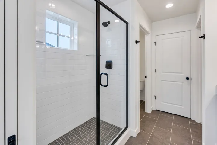 Glass-enclosed shower with black trim, white horizontal tiling, and a small square window