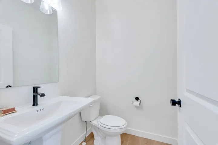 Pedestal sink with a matte black faucet, wall-mounted mirror, and overhead lighting