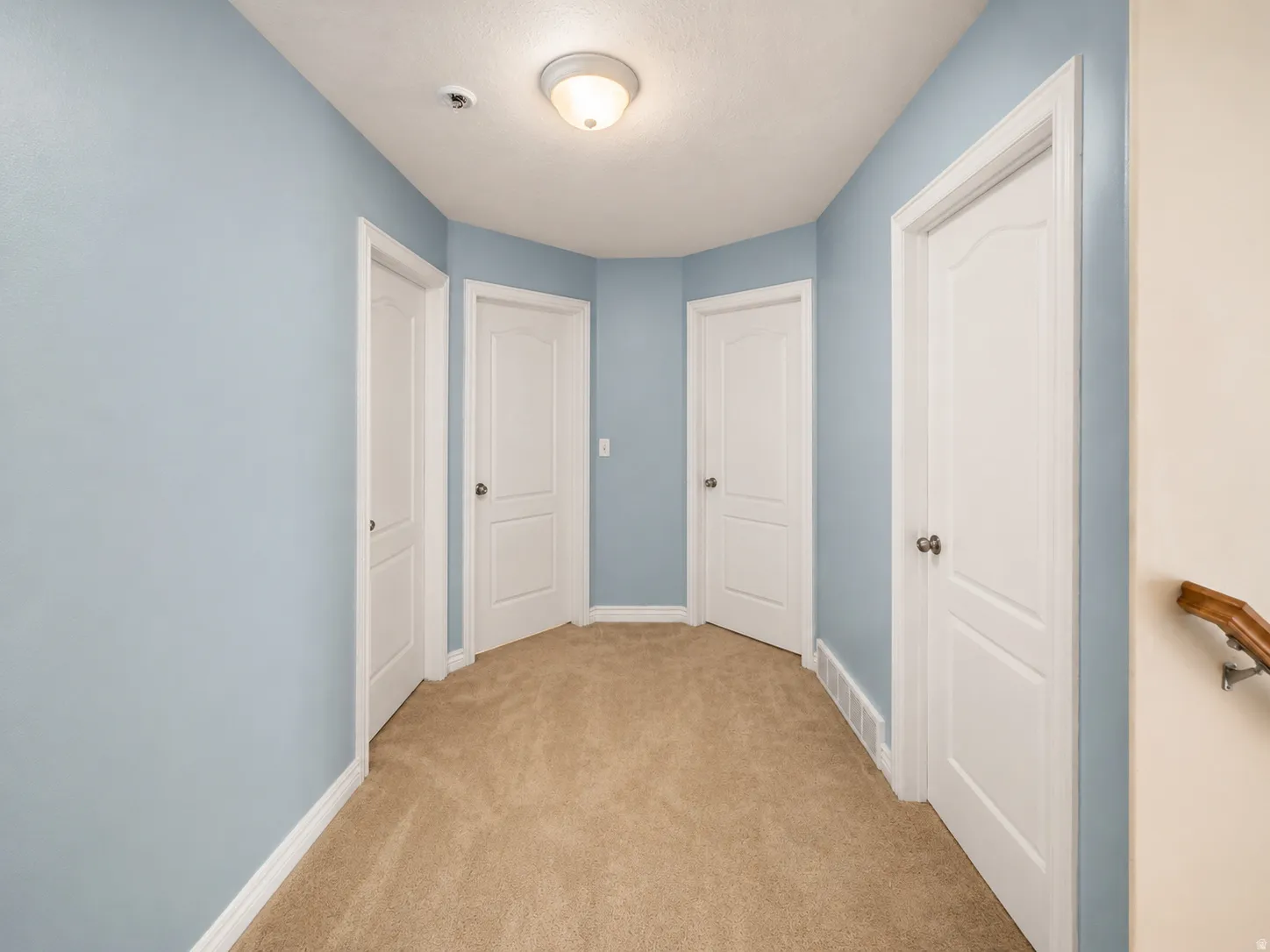Hallway featuring light blue walls, tan carpeting, and multiple white paneled doors