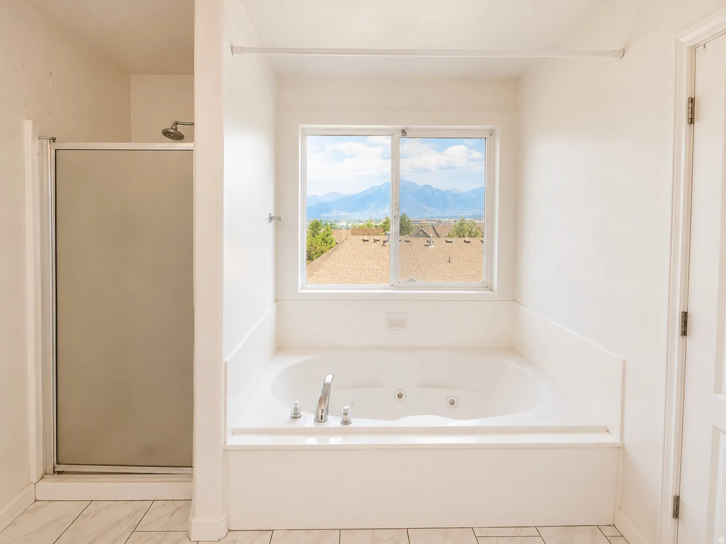 Jetted soaking tub with a window, white tile flooring, and a separate shower with a glass enclosure