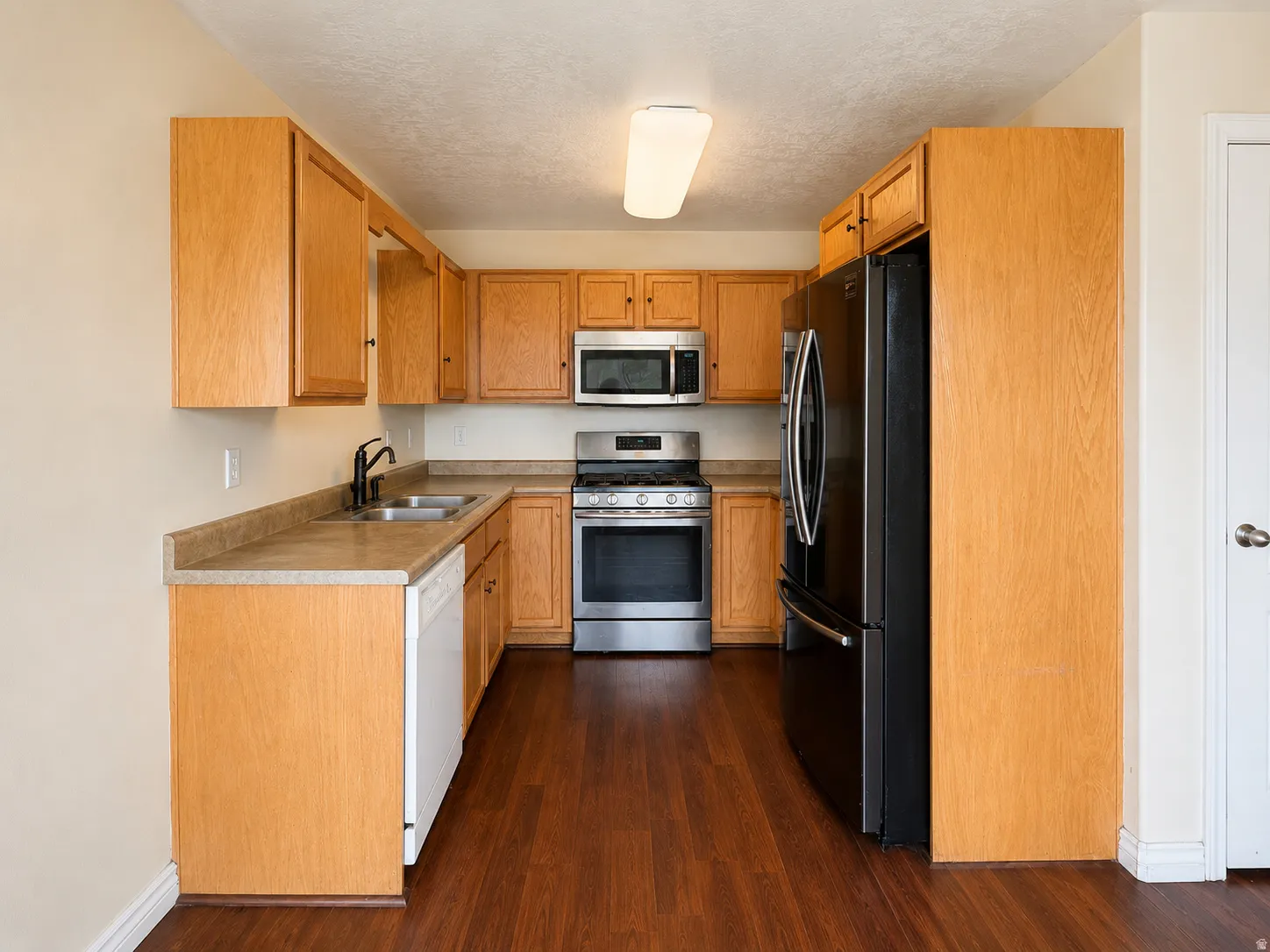 U-shaped kitchen with wood-finish flooring, light wood cabinetry, stainless steel appliances, and a double basin sink with a matte black faucet
