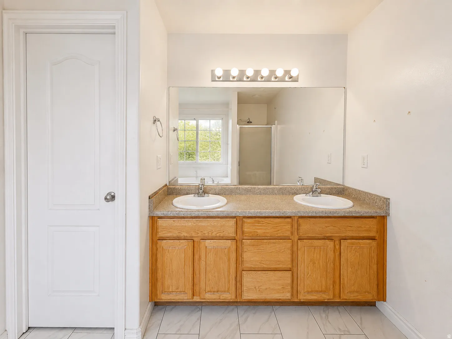 Dual vanity with integrated sinks, wood-finish cabinetry, and a large wall-mounted mirror