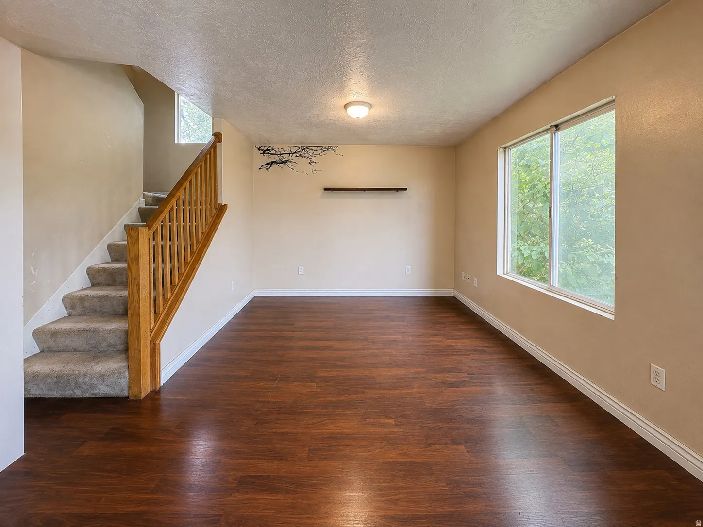 Wood-finish flooring, staircase with carpeted treads and wood handrail, ample natural light from a large window, recessed wall shelving, and a ceiling-mounted fixture