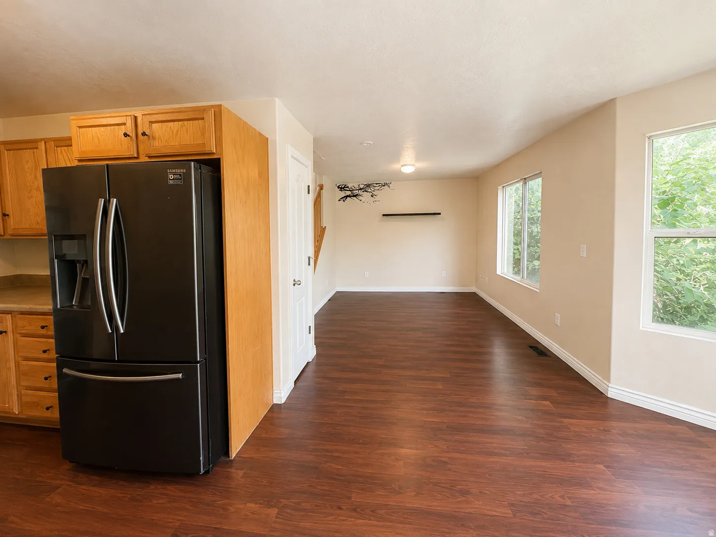 Open-concept living area featuring wood-finish flooring, multiple windows, and a black refrigerator