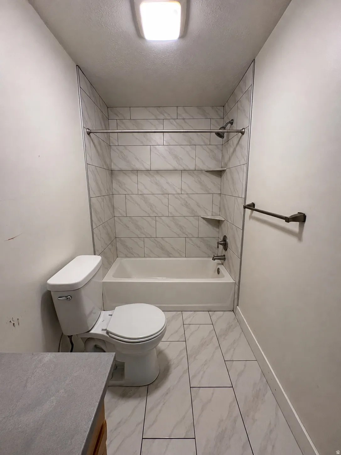 Bathtub with tile surround and built-in shelving, white toilet, and tile flooring