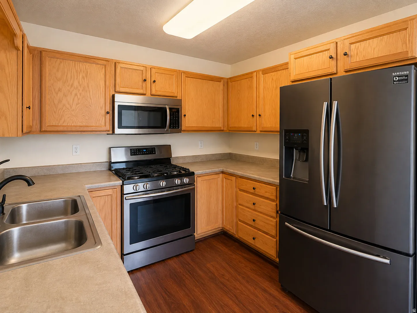 Kitchen featuring wood-finish flooring, light wood cabinetry, stainless steel sink, and stainless steel range with microwave