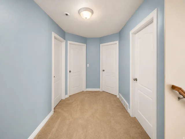 Hallway featuring light blue walls, tan carpeting, and multiple white paneled doors