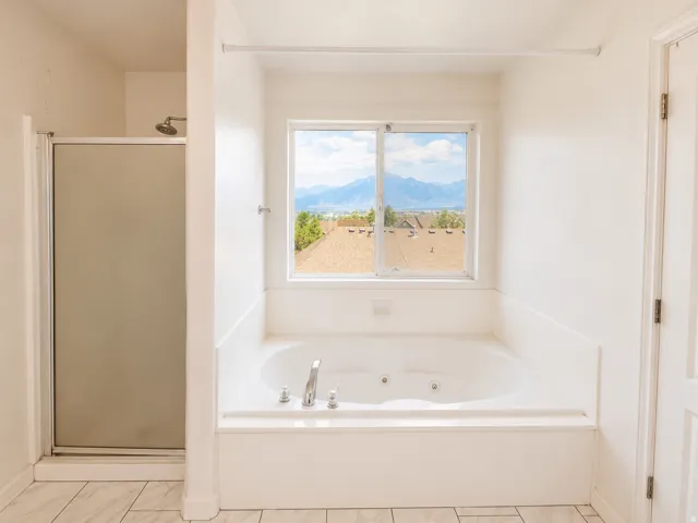 Jetted soaking tub with a window, white tile flooring, and a separate shower with a glass enclosure