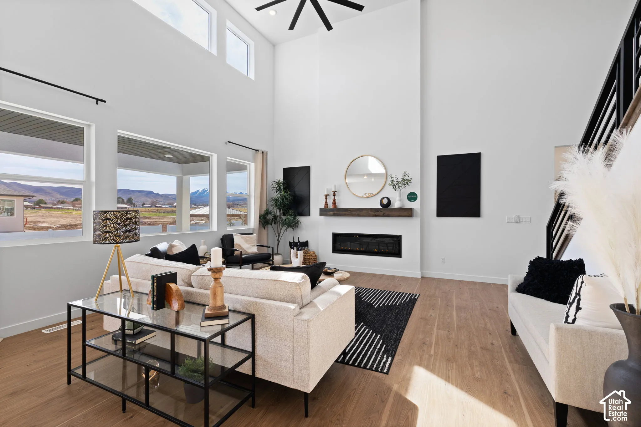 Double-height ceiling with clerestory windows, large picture windows, wood-finish flooring, linear electric fireplace with wood mantel, and an open-tread staircase with metal railings