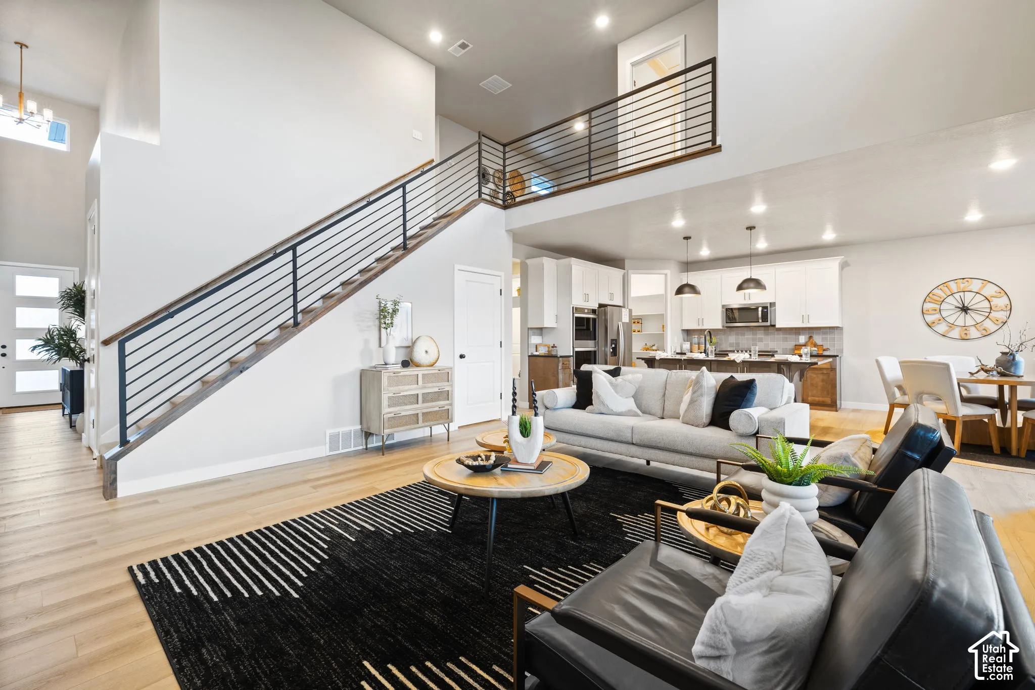 Open-concept living area with high ceilings, wood-finish flooring, and a contemporary staircase with metal railings