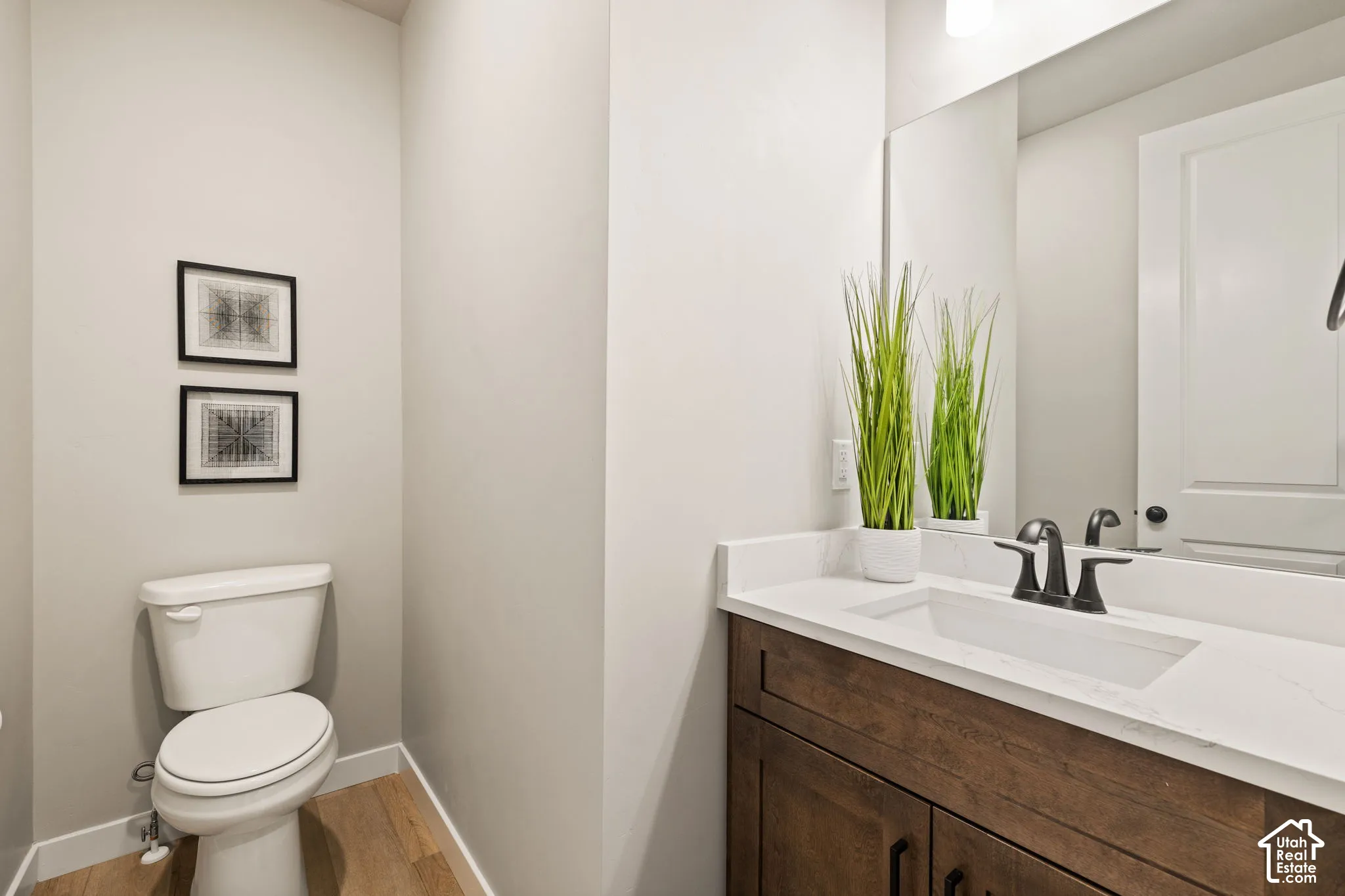 Wood-finish flooring, white toilet, dark wood-tone vanity with cabinet storage, integrated sink, and a large wall mirror