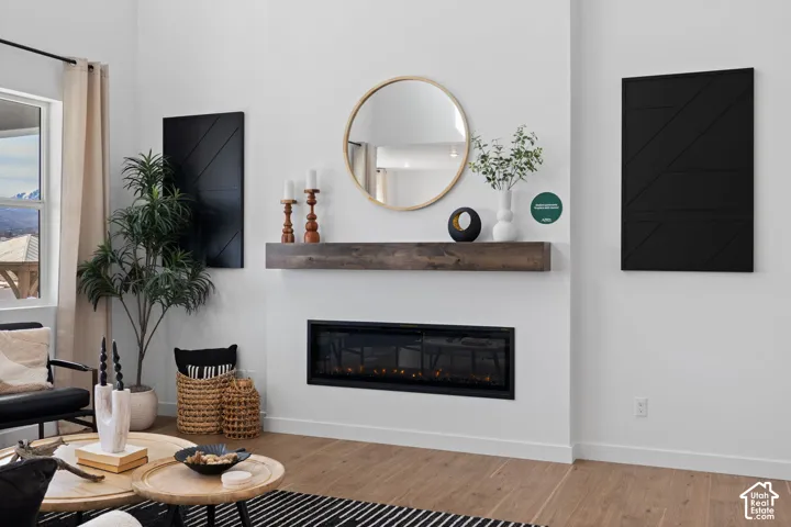 White walls with wood-finish flooring, a linear electric fireplace, and a wood mantel