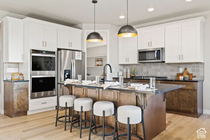 Kitchen featuring two-tone cabinetry, stainless steel appliances, a center island with seating, a tile backsplash, and recessed lighting