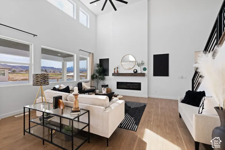 Double-height ceiling with clerestory windows, large picture windows, wood-finish flooring, linear electric fireplace with wood mantel, and an open-tread staircase with metal railings