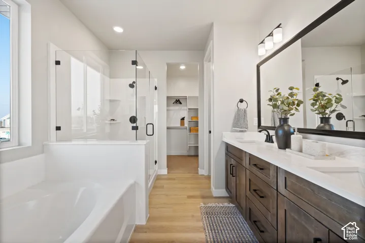 Spacious bathroom featuring a double vanity with stone countertops, wood-finish cabinetry, a large frameless glass shower, a soaking tub, and recessed lighting