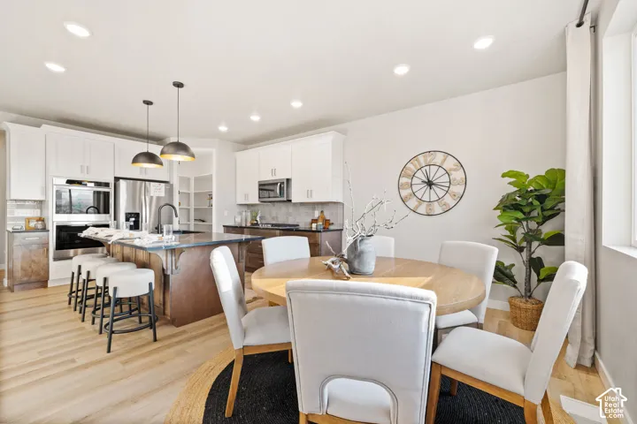 Open-concept kitchen and dining area featuring light wood-finish flooring, white cabinetry, recessed lighting, a kitchen island with pendant lighting, and stainless steel appliances