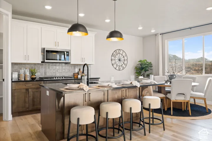 Open-concept kitchen and dining area featuring a kitchen island with seating, stainless steel appliances, two-tone cabinetry, and wood-finish flooring
