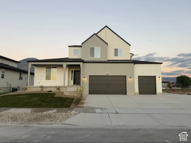 Two-story exterior featuring multi-material siding, stacked stone accents, a covered porch, a three-car garage, and mountain backdrop