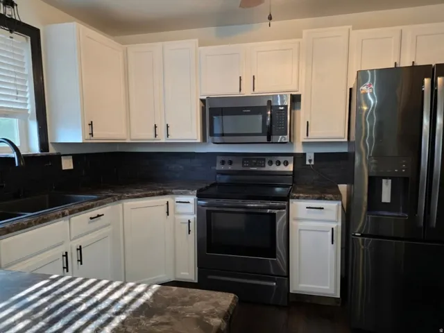 Modern kitchen featuring cream-colored cabinetry with hardware accents, black stainless steel appliances including a slide-in range and over-the-range microwave, dark countertops with contrasting edge detail, and black subway tile backsplash