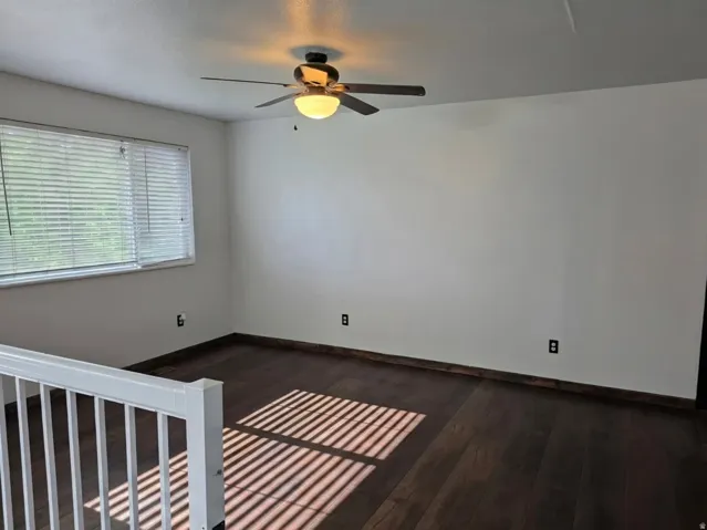 Wood-finish flooring, white painted walls, ceiling fan with integrated lighting, and a white railing