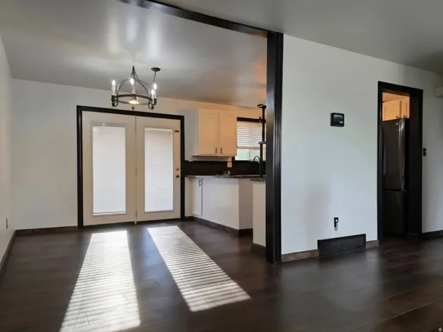 Open-concept living and kitchen space featuring dark wood-finish flooring, black-framed glass French doors with transom windows, stainless steel appliances, light cabinetry, and a modern pendant light fixture