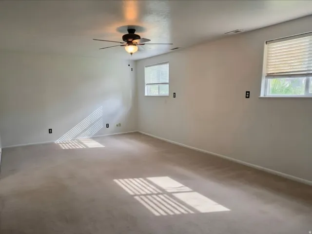Spacious room with light-colored carpeting, multiple windows, and a ceiling fan