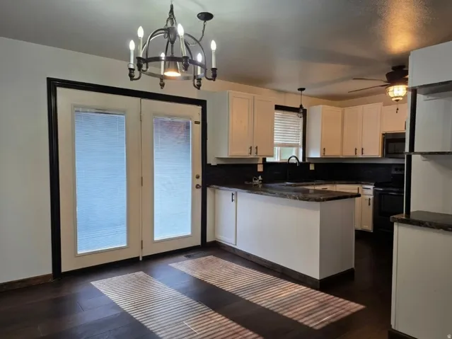 Modern kitchen featuring white cabinetry with black hardware, dark countertops, and stainless steel appliances