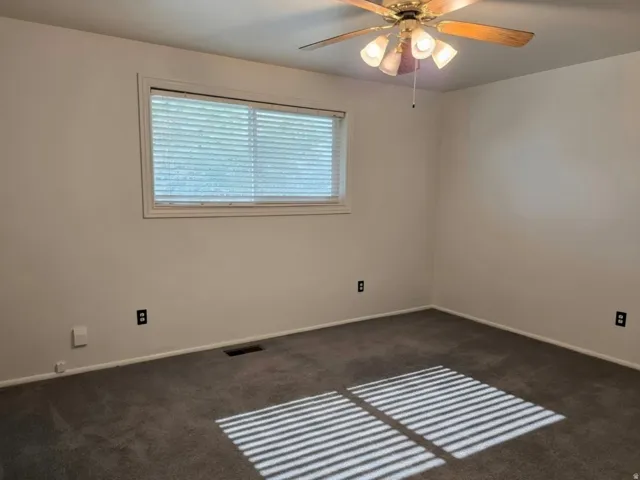 Spacious bedroom with neutral wall finishes, dark carpet flooring, and abundant natural light from a large horizontal window