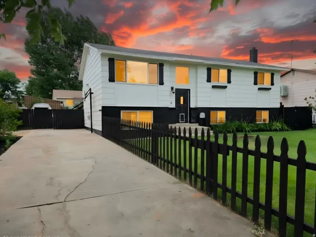 White exterior with black trim, concrete driveway, black picket fence, and a manicured lawn