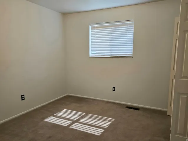 Bright, neutral bedroom featuring neutral wall finishes, carpet flooring, and abundant natural light from a large window with horizontal blinds