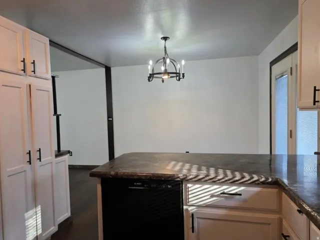 White cabinetry with matte black hardware, dark countertops, dark wood-finish flooring, and a black chandelier