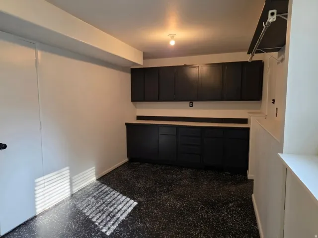 Finished Garage Space with Dark Cabinetry and Granite CountertopThis garage features extensive dark cabinetry storage lining the walls, a granite countertop work surface, and concrete flooring