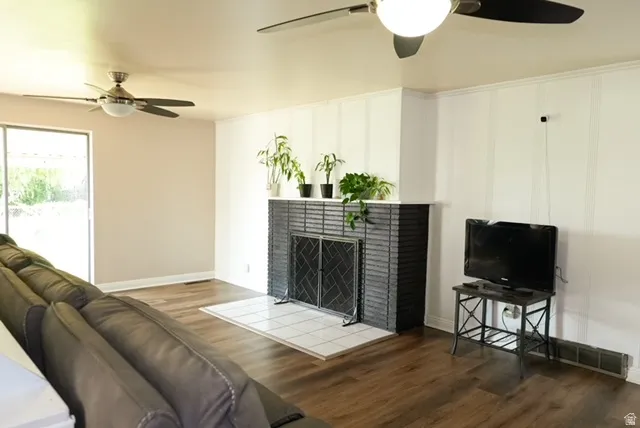 Wood-finish flooring throughout, white board and batten accent wall, black brick fireplace with a white tile hearth, ceiling fans with integrated lighting, and a sliding glass door