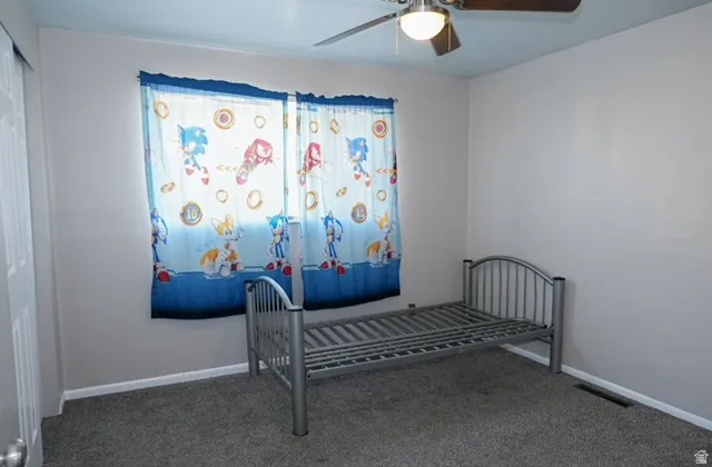 Ceiling fan with integrated lighting, window with light-filtering curtains, carpeted flooring, and a permanent closet with a bi-fold door